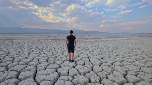 Young Adult Standing on Cracked Lakebed at Sunset