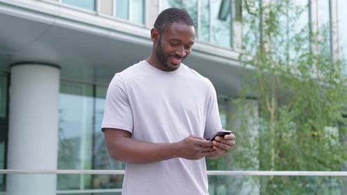 African American Man Holding Smartphone Touch Screen Typing Scroll Page on Urban Street in City Guy