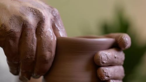 Male potter hands shaping raw clay vase neck close up on pottery turntable wheel