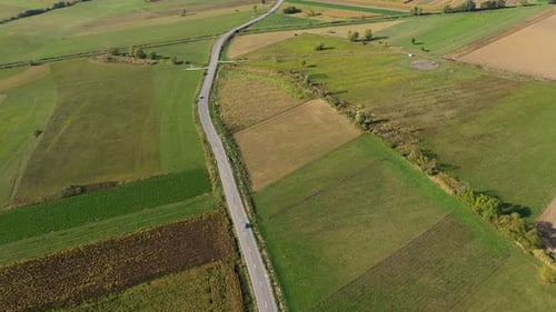 Flying Above a Countryside Road Following a Car Among Agriculture Fields by Drone
