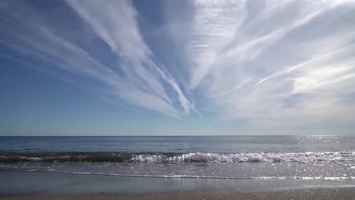 Footage shows gorgeous ocean sea water waves hitting a sandy beach shoreline during a sunny day whil