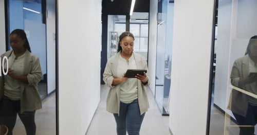 Happy african american casual businesswoman using tablet walking in office corridor, slow motion