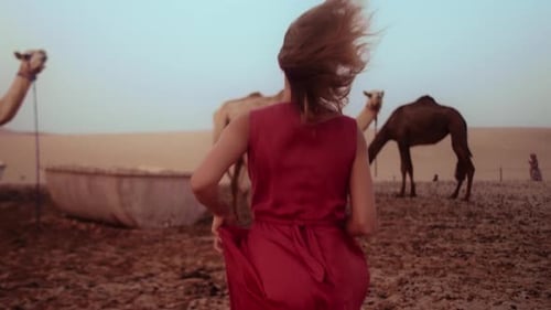 Beautiful girl wearing red dress running barefoot on the sand in the desert of united Arab emirates