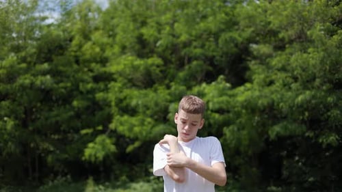 Dissapointed Kid Touching Painful Area on Arms While Standing Near Greenery