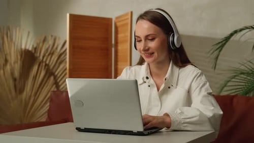Woman works on laptop with headphones indoors