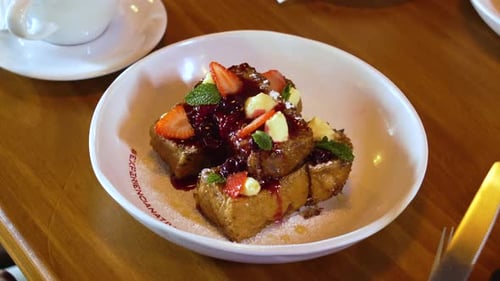 Close-Up of Golden French Toast Bites with Strawberries and Berry Sauce in White Ceramic Bowl at Caf