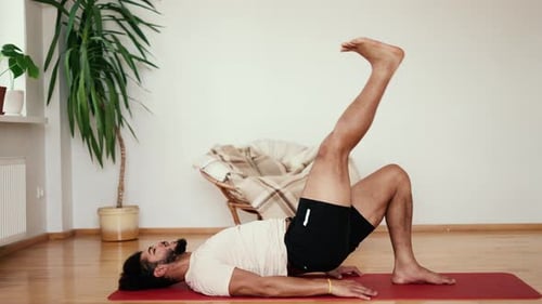 Sportsman with Black Hair Exercises Lifting His Leg Up in the Living Room