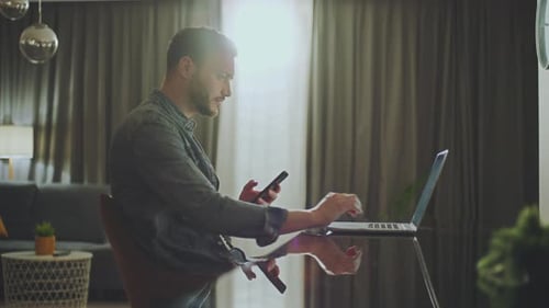 Man Using Phone and Laptop at Home