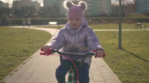 Portrait Cute Smiling Girl Riding Bicycle in Sunny Winter in City Park at Beautiful Sunset in Slow