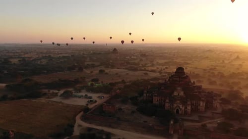 Ancient Buddhist temple in Bagan, Myanmar with dozens of hot air balloons in background during sunri