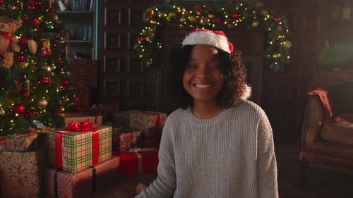 Smiling Young Woman Wearing Santa Hat near Christmas Tree