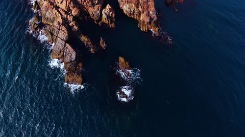 Deep blue water hits the bare rocks. Aerial perspective on the foamy waves splashing
