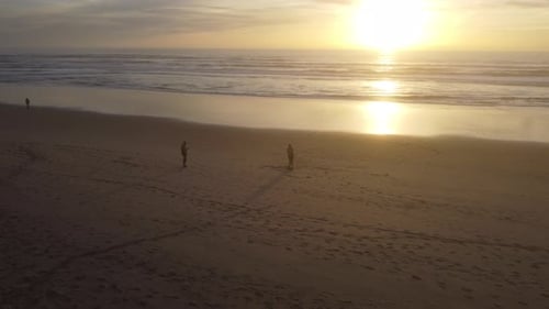 Dronie shot (flying up and away from the subject), of a man on a beach with a sunset in the backgrou