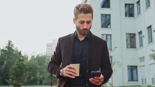 Man in Suit Checks Phone While Sipping Coffee Outside Office