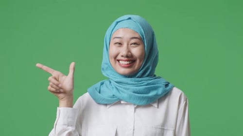 Close Up Of Asian Muslim Woman Smiling And Pointing To Side While Standing In The Green Screen