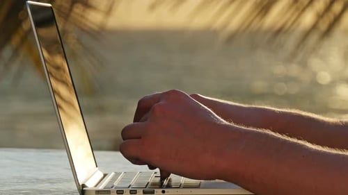 Man Typing on a Laptop on the Beach at Sunrise Beach