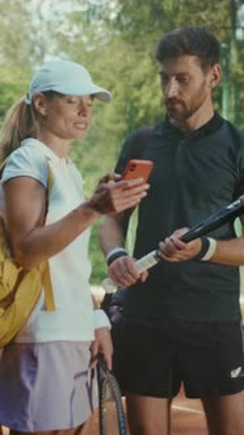 Woman Shows Phone to Bearded Man on Tennis Court