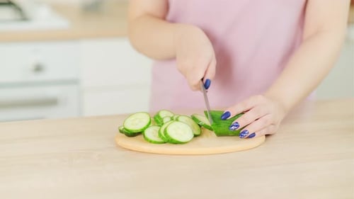 Woman Slices Cucumber on Cutting Board