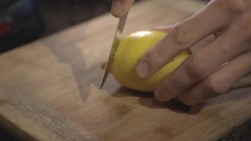 Una persona corta lentamente con las manos un limón recién rasgado en una tabla de cortar - Foto de cerca