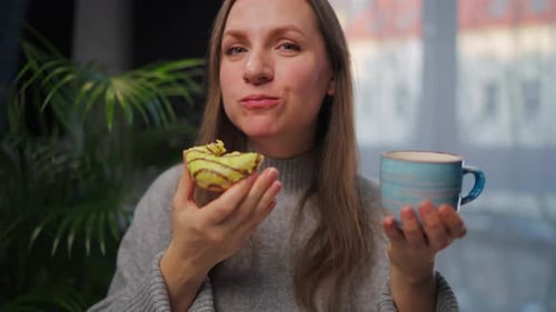 Woman Eats Pastry and Drinks from Mug Indoors