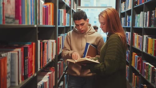 Two Students Discussing a Book in a Library Aisle