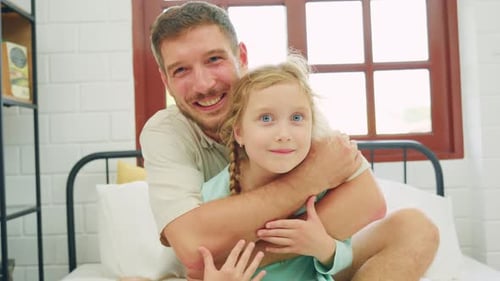 Smiling Man Hugging Little Girl on Bed