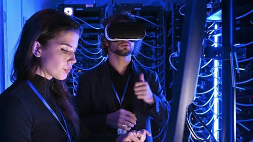 Woman programming in a server room while a man is using a Virtual Reality headset