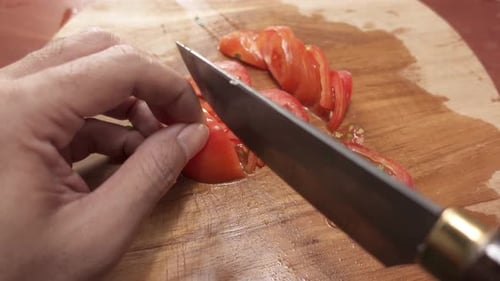 Close-up of slicing ripe red tomatoes into thin slices with a kitchen knife on a cutting board