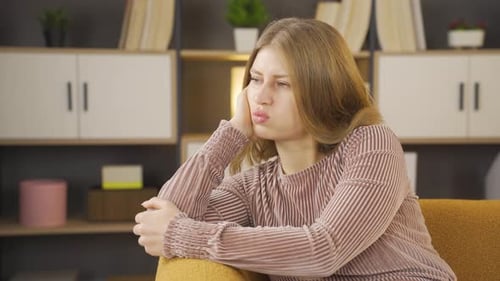 Sad Woman Sits on Sofa with Head in Hand