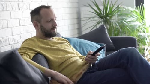 Man Relaxing on Couch, Using Remote Control