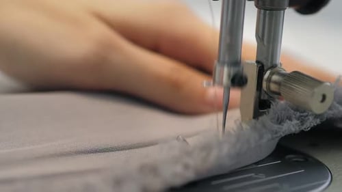 Close Up Slow Video of Woman's Hand Sews Grey Fabric on a Professional Sewing Machine at the