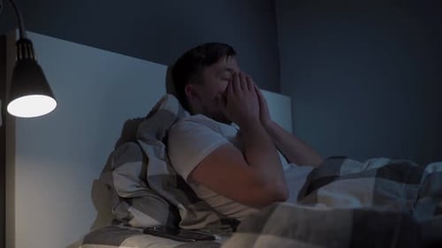 Man Lying in Bed at Night, Rubbing His Face