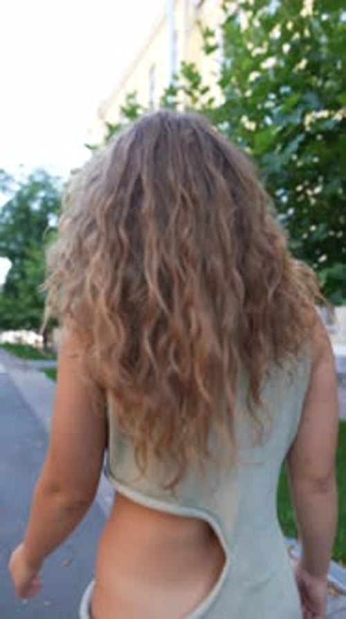 A Beautiful Girl with Curly Hair is Walking the Streets of the City on a Summer Day