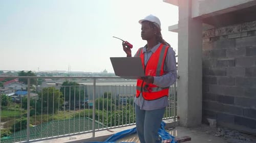 Young engineer walking inspection construction site and speak on talkie walkie and looking laptop.