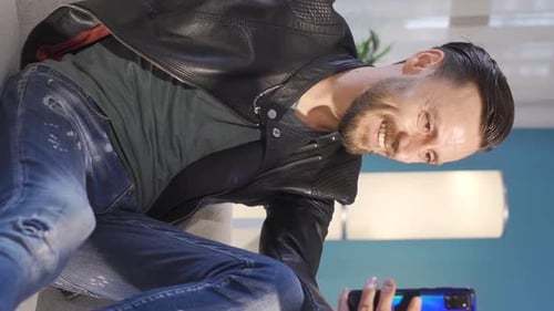 Vertical Video of Happy and handsome young man texting, smiling, enjoying using his smartphone.