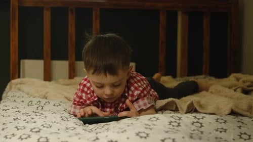 Child Playing Smartphone on Quilted Bed at Home
