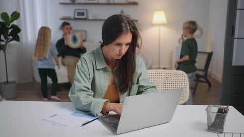 A Business Woman Works Remotely at Home on a Laptop While Her Family is Singing in the Background
