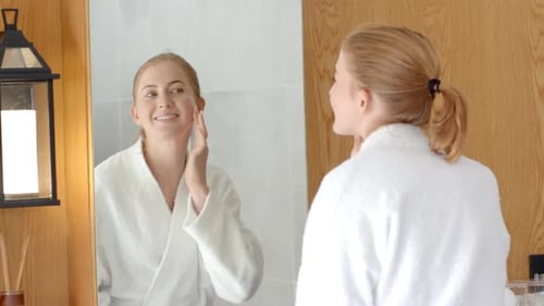 Woman Applying Moisturizer in Bathroom Mirror