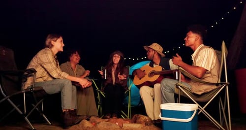 Friends Play Guitar at Campfire at Night