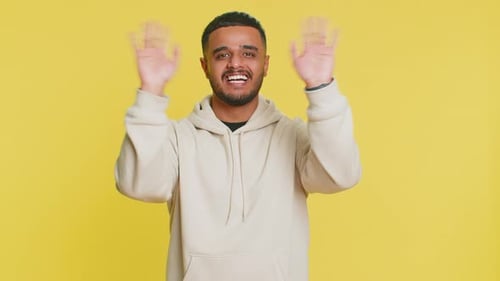 Enthusiastic Young Adult Waving Hello on Yellow Background