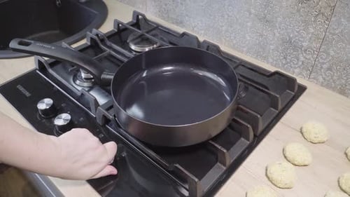 A woman's hand lights the gas under the pan and pours oil on it