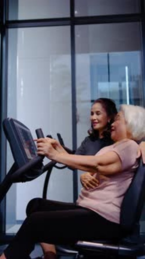 Happy senior Asian women exercising in a gym, a trainer helps an elderly woman with the stationary