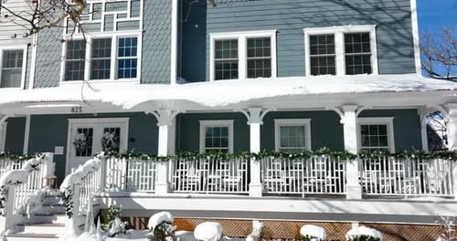 Blue apartment building in winter snow. Icicles hang from snowy roof. Winter snow with Christmas dec
