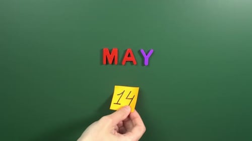 Hand sticking a sticker 14 May calendar day on school board. 14 date of May. Fourteenth day May