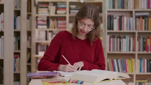Foto eines weißen Mädchens mit Brille, das in der Bibliothek studiert, Halbkörperaufnahme