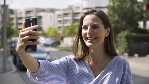 A Beautiful Young Caucasian Woman Shoots a Vlog with Her Smartphone in a Street in an Urban Area