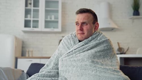 Homme malade recouvert d'une couverture chaude. Le jeune homme a de terribles maux de tête et se sent mal à la maison.