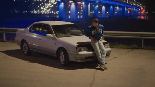 Nighttime Waterfront Scene Featuring Man Near Neonlit Bridge and Parked Vehicle Solitary Man Leans