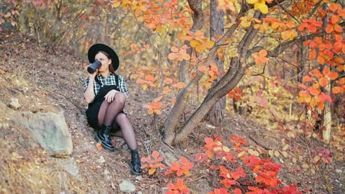 Hipster Woman Drinking Hot Coffee or Tea Thermos Golden Park Forest in Autumn