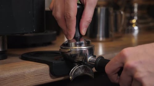 Closeup of a Barista Tempering Ground Coffee with a Tempera in a Coffee Shop